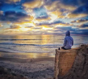 A serene scene of a person sitting on a rock, gazing at the sunset over a calm sea, reflecting the mindfulness and introspection often encouraged in counselling sessions.